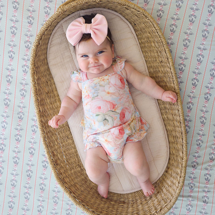 baby wearing a floral romper in a wicker basket