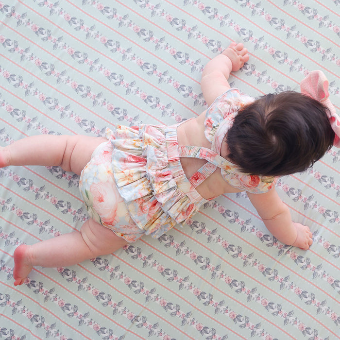 back image of baby wearing a floral romper laying on a patterned floor