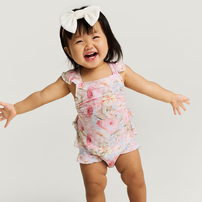 baby wearing a floral romper with white hair bow on a white background