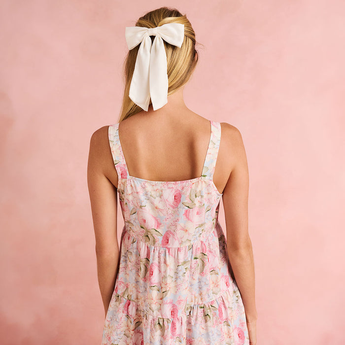 Woman wearing a floral dress with a white bow in her hair against a pink background