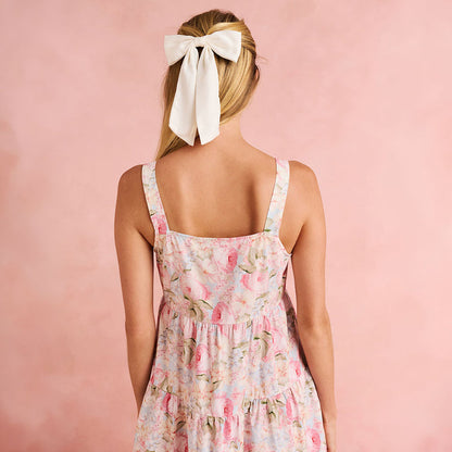 Woman wearing a floral dress with a white bow in her hair against a pink background