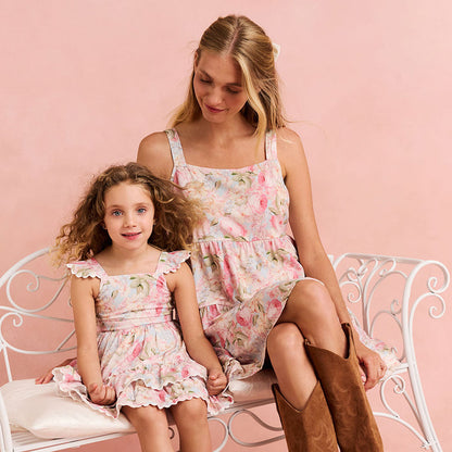 Woman and young girl sitting on a bench wearing matching floral dresses against a pink background