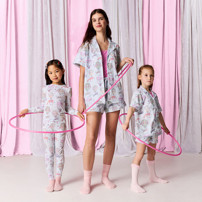 Woman and two children in matching pajama sets with pink hula hoops against a pink and gray curtain background.