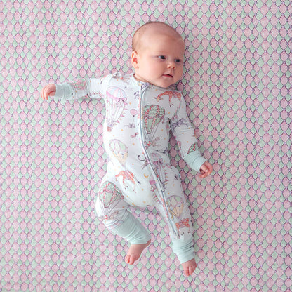 Baby lying on a patterned pink and green blanket wearing a onesie with colorful designs.