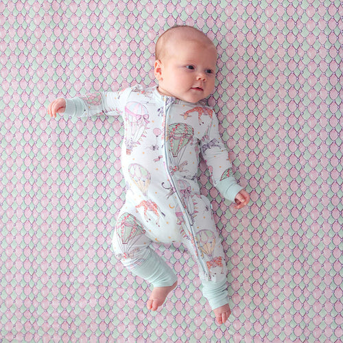 Baby lying on a patterned pink and green blanket wearing a onesie with colorful designs.