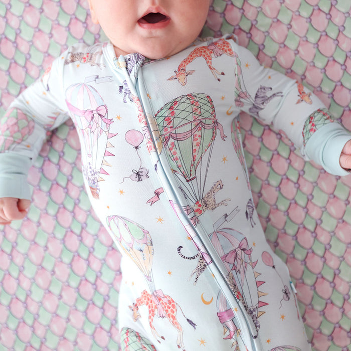 Baby in a onesie with hot air balloon pattern on a pink and green textured blanket