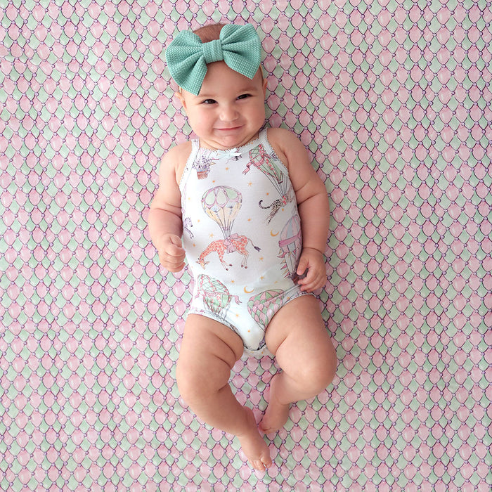 Baby wearing a patterned bodysuit and headband on a pink and green textured background