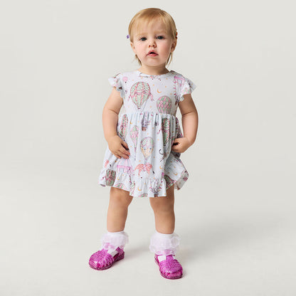 Child wearing a circus print dress with pink shoes on a plain background
