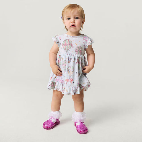 Child wearing a circus print dress with pink shoes on a plain background