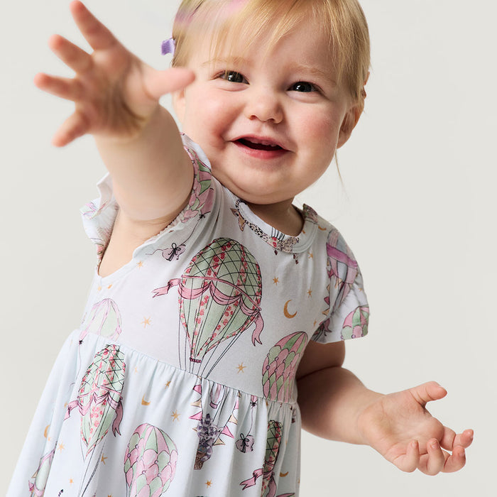 Child wearing a dress with a pattern of elephants and other animals on a plain background