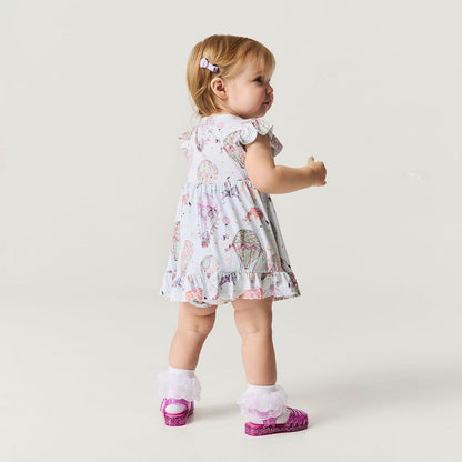 Child wearing a circus print dress and pink shoes on a plain background