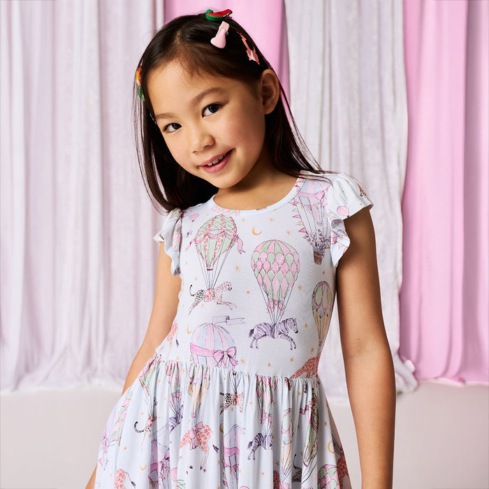 Young girl wearing a dress with hot air balloon pattern against a pink curtain background