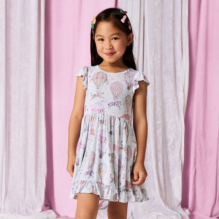 Girl wearing a circus printed dress against a white and pink curtain