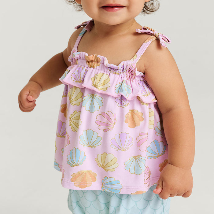 Baby wearing a pink top with shell pattern and light blue shorts on a white background