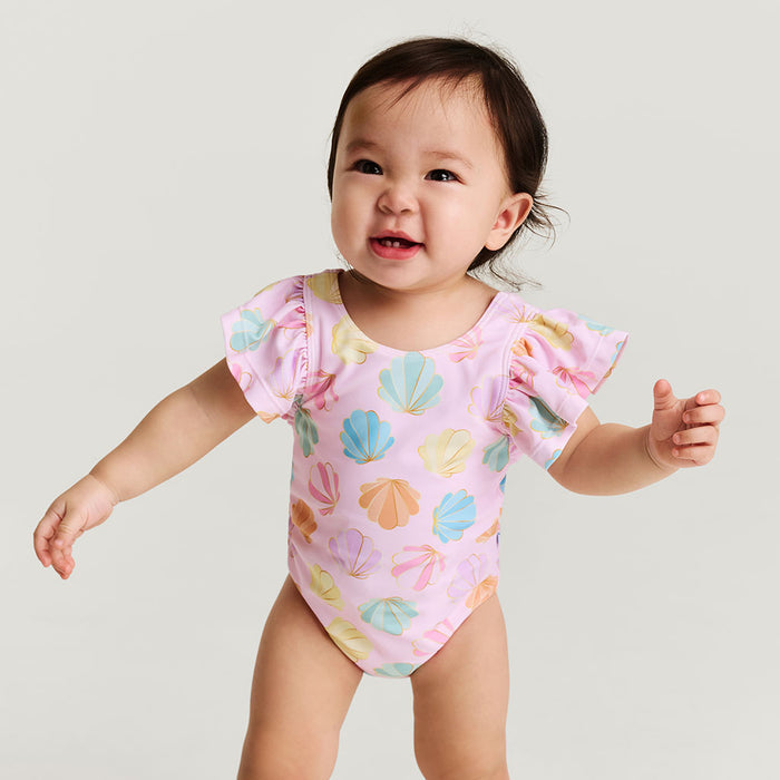 Baby wearing a pink swimsuit with shell pattern on a plain background
