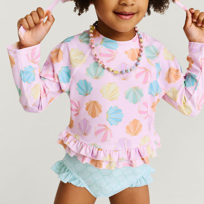 Child wearing a colorful shell-patterned rash guard and light blue shorts on a plain background