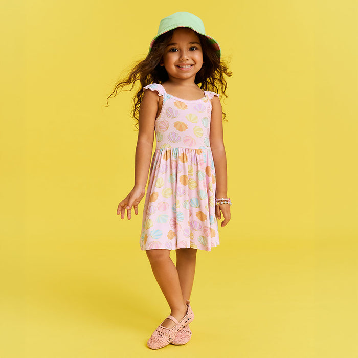 Young girl in a shell patterned dress and hat on a yellow background