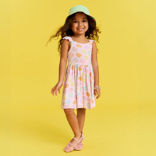 Young girl in a shell patterned dress and hat on a yellow background