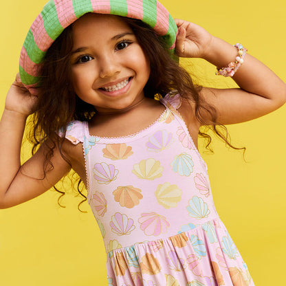 Young girl wearing a colorful dress with shell patterns and a matching hat on a yellow background