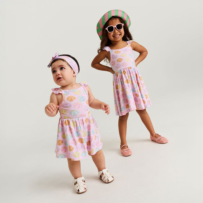 Two young girls wearing matching dresses with a white background
