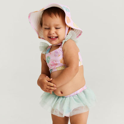 Child wearing a floral top and tutu skirt with a matching hat on a light gray background