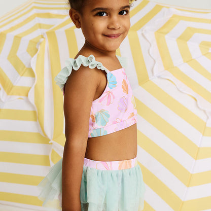 Young girl wearing a colorful top and light blue tulle swim skirt against a striped background