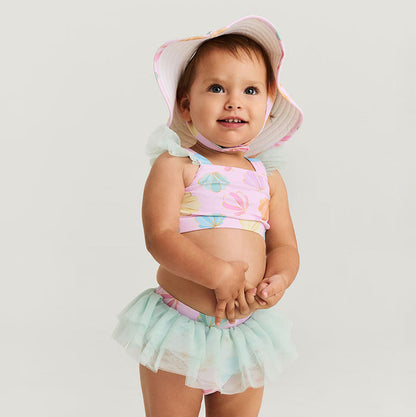 Baby wearing a colorful floral bikini and matching hat on a light gray background
