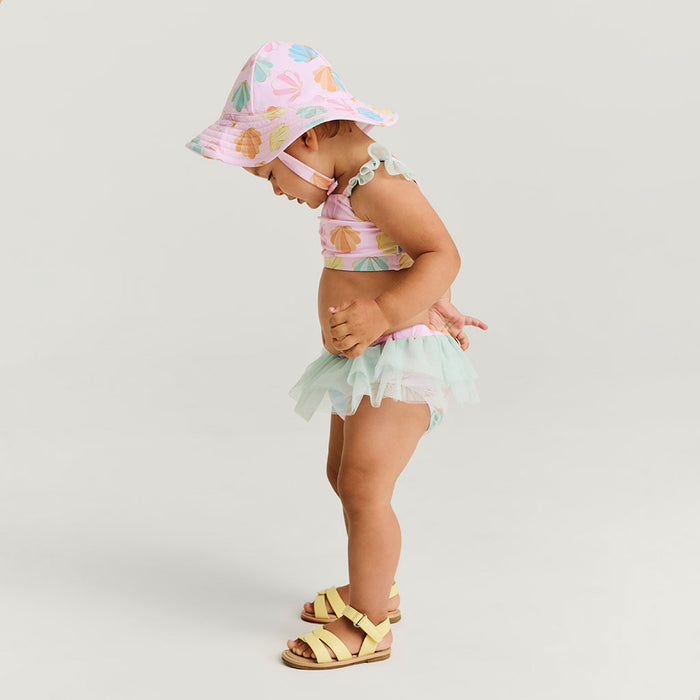 Child wearing a colorful hat, swimsuit, and sandal on a plain background