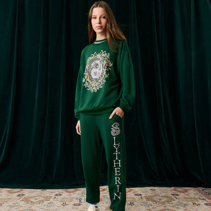 Person wearing a green Slytherin-themed jogger set with a dark green curtain background