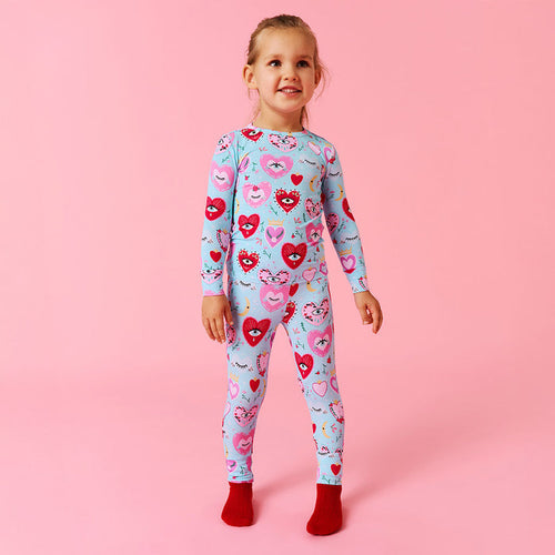Child wearing a colorful heart-patterned pijama set on a pink background