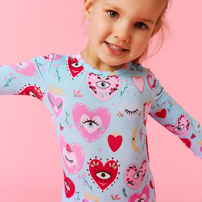 Child wearing a colorful patterned pijama with hearts and eyes on a pink background