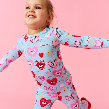 Child wearing a light blue one piece with heart and face patterns on a pink background