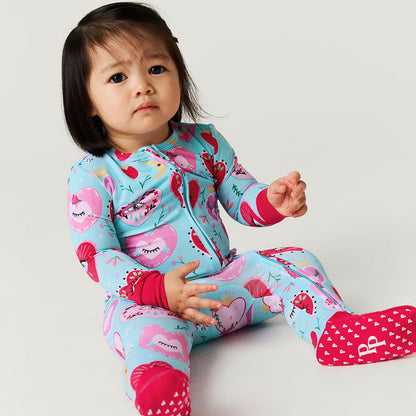 Child wearing a colorful one piece with heart and eyes pattern on a light gray background