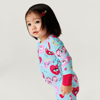 Child wearing a colorful one piece with heart and eyes prints on a plain background