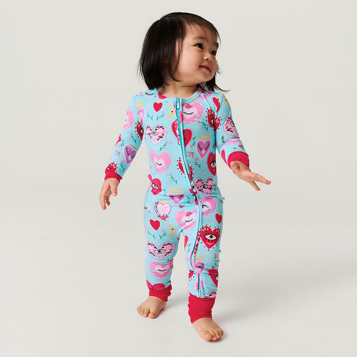 Baby wearing a colorful one piece with heart and eyes pattern on a plain background