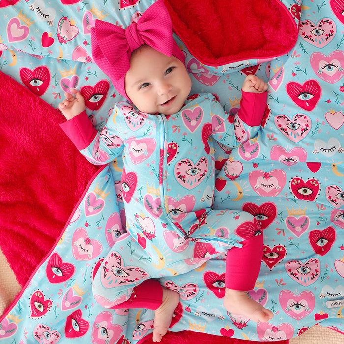 Baby in a colorful one piece with heart and eyes pattern on a matching blanket