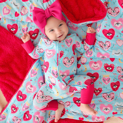 Baby in a colorful one piece with heart and eyes pattern on a matching blanket