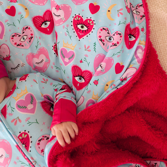 Child wrapped in a blue and red plush blanket with heart-patterned fabric
