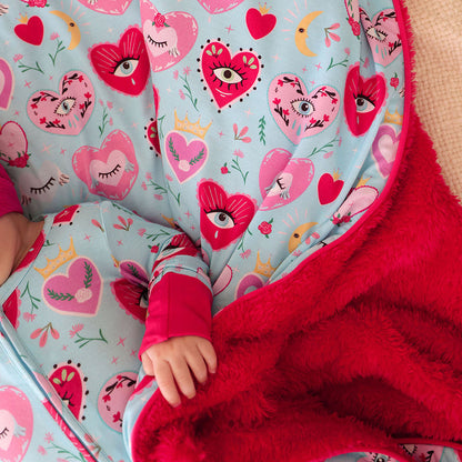Child wrapped in a blue and red plush blanket with heart-patterned fabric