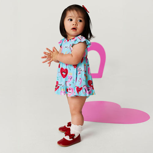 Child wearing a colorful dress with hearts and red shoes on a light gray background