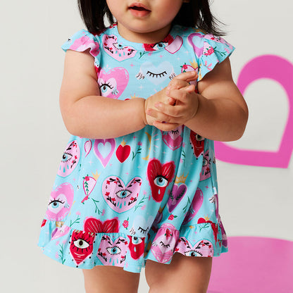 Close up detail of a child wearing a colorful dress with heart and eye patterns against a pink and white heart background.