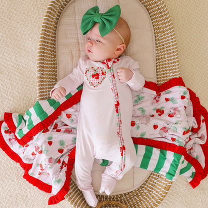 Baby wearing a bamboo viscose one piece with solid light pink fabric and strawberry printed side applique, laying on a matching blanket in a woven bassinet.