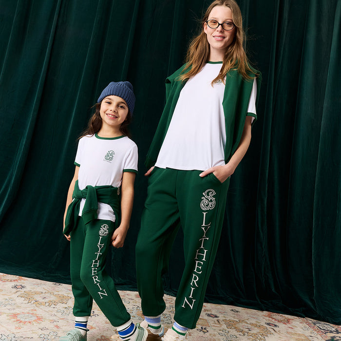 Two people wearing matching Slytherin-themed clothing in front of a green curtain.