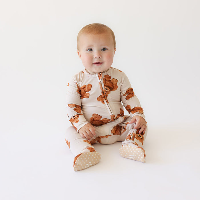 Baby wearing a brown and white patterned one piece on a white background