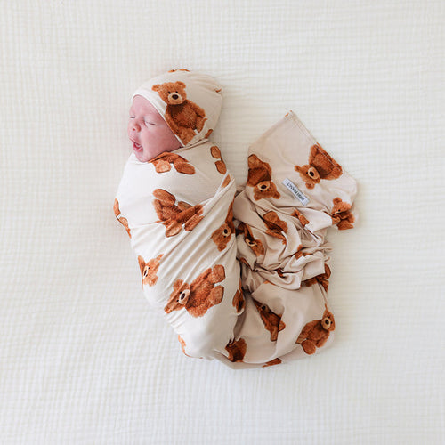 Newborn baby wrapped in a bear-patterned swaddle on a white background