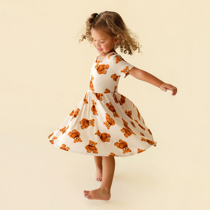 Child wearing a dress with teddy bear pattern on a beige background