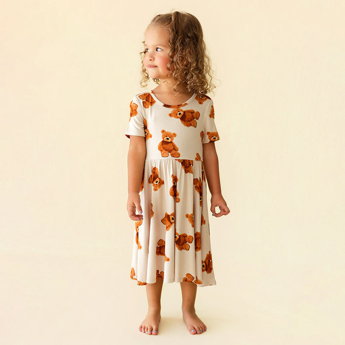 Young girl wearing a white dress with brown teddy bear patterns on a beige background