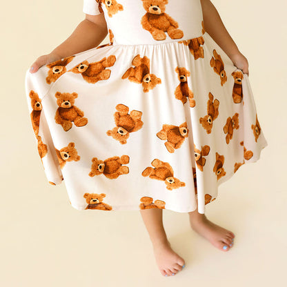 Child wearing a dress with teddy bear pattern on a plain background