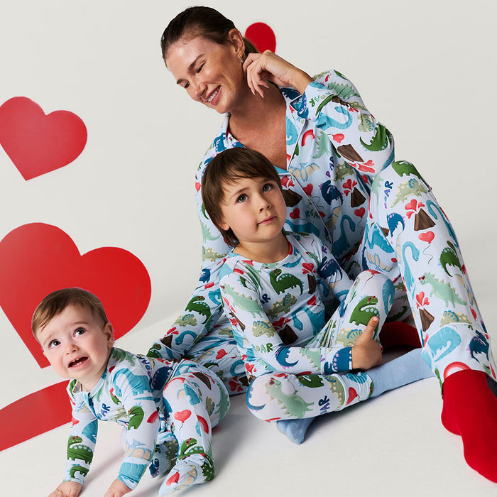 Woman and two children wearing matching dinosaur pajamas with a heart-themed background