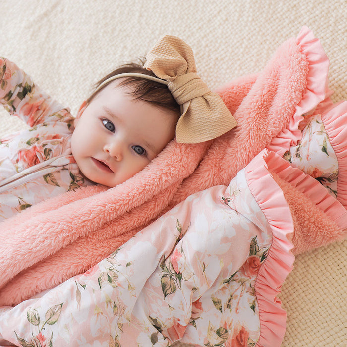 Baby wrapped in a pink floral blanket with a large bow on a light background